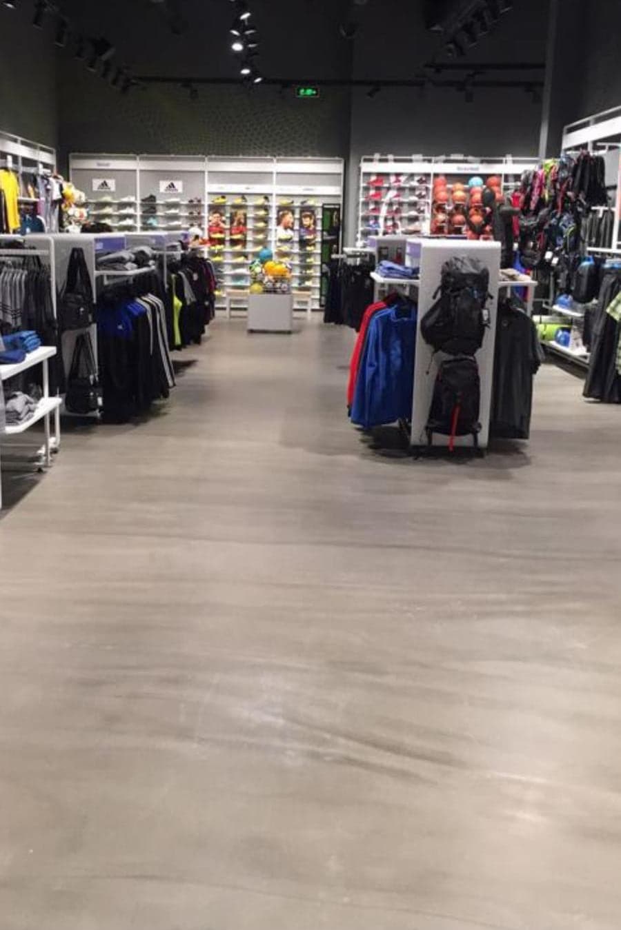 Spor mağazası reyonları arasında açık gri dekoratif şap; tavan spotlarının ışığı yüzeyde yumuşak lekeler halinde