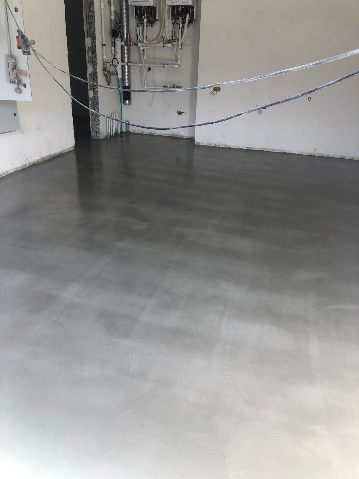 Boş bir mekânda yeni uygulanmış gri mikro beton zemin; duvarda henüz bağlanmamış elektrik tesisatı