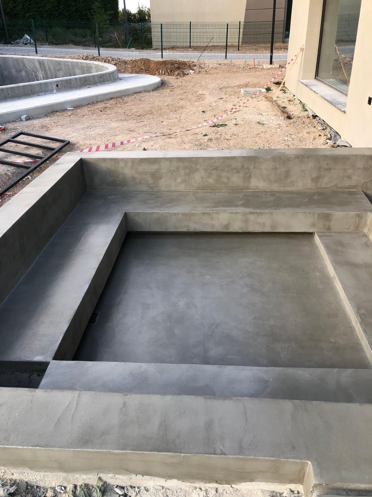 Dış mekânda mikro beton kaplı basamaklar ve basamaklı çukur; arkada henüz düzenlenmemiş toprak alan