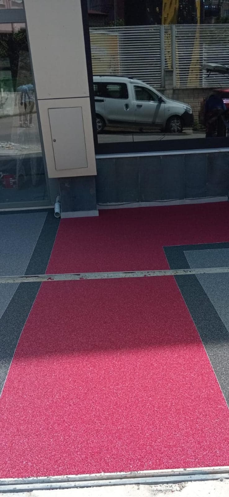 Bina girişinde gri taş halı içine işlenmiş kırmızı yürüyüş yolu